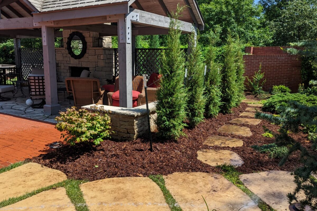image (7) Flagstone stepping stones past an arborvitae privacy screen to a pavilion with a stone fireplace